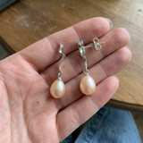 Boucles d'oreilles argent 925 pendantes avec perles de culture roses, tenues dans une main.