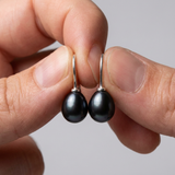 Boucles d'oreilles argent 925 et perles de culture noires Tahiti tenus entre les doigts.