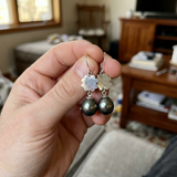 Boucles d'oreilles argent 925 trèfle avec perles noires, tenues entre les doigts.