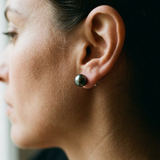 Boucles d'oreilles bouton en or blanc 9 carats avec perle de Tahiti noire portées à l'oreille.