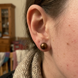 Boucles d'oreilles bouton en or jaune avec perle de culture chocolat portées à l'oreille.