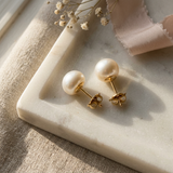 Boucles d'oreilles bouton en or jaune 9 carats serties de perles de culture blanches, posées sur marbre.