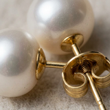 Gros plan sur le système de fermoir à vis en or jaune de boucles d'oreilles bouton perles blanches.