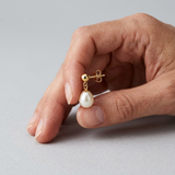 Boucles d'oreilles or blanc 9 carats avec perle de culture blanche pendante, tenues en main.