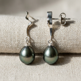 Boucles d'oreilles pendantes or blanc 9 carats avec perles de Tahiti noires sur tissu beige.