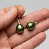 Boucles d'oreilles en or jaune 9k avec perles de culture poire vertes, présentées dans une main.
