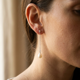 Boucles d'oreilles pendantes en or blanc 9 carats avec chaîne et perle blanche, portées à l'oreille.
