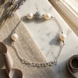 Bracelet en argent 925 avec perles de culture blanches et bille pavée de strass, posé à plat.