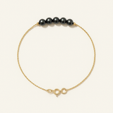 Bracelet or jaune 9 carats avec cinq perles noires sur chaîne fine et fermoir anneau.