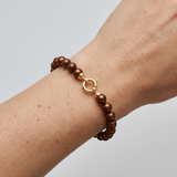 Bracelet perles chocolat et fermoir anneau en or jaune 9 carats porté au poignet.