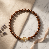 Bracelet perles chocolat et fermoir anneau en or jaune 9 carats, posé à plat.