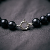 Gros plan sur le fermoir anneau argenté d'un bracelet en perles noires.