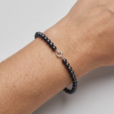 Bracelet perles noires et fermoir en or blanc 9 carats porté au poignet.