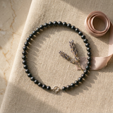 Bracelet perles noires et fermoir en or blanc 9 carats posé à plat sur lin beige.