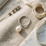 Créoles en argent 925 avec perle de culture blanche pendante, posées sur lin beige.