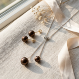 Collier lasso et boucles d'oreilles à perles chocolat sur chaîne argentée, fond lin naturel.