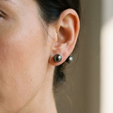 Puces d'oreilles en or blanc et perles de Tahiti noires portées à l'oreille.