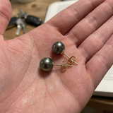 Puces d'oreilles en or jaune avec perles de Tahiti grises présentées dans une paume de main.